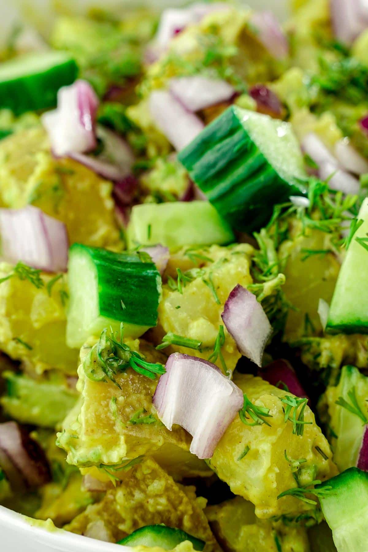 cucumber and red onions on top of avocado potato salad