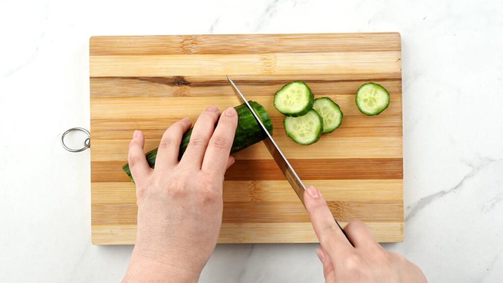 knife slicing cucumber on cutting board