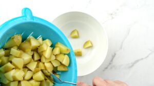 teal colander of potatoes above white plate