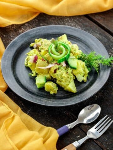 round black plate of vegan potato salad on table by yellow napkin