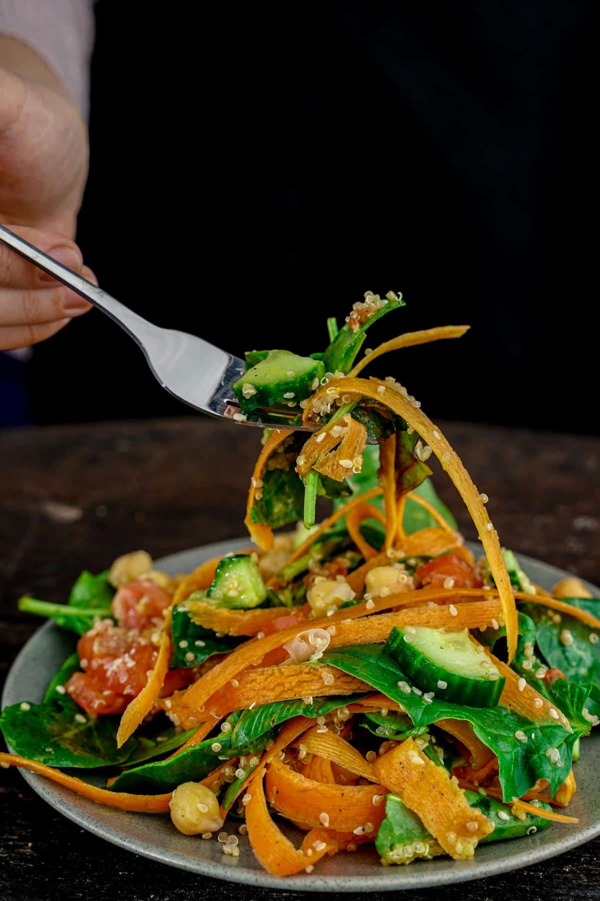 fork of rainbow salad held above a gray plate with black background