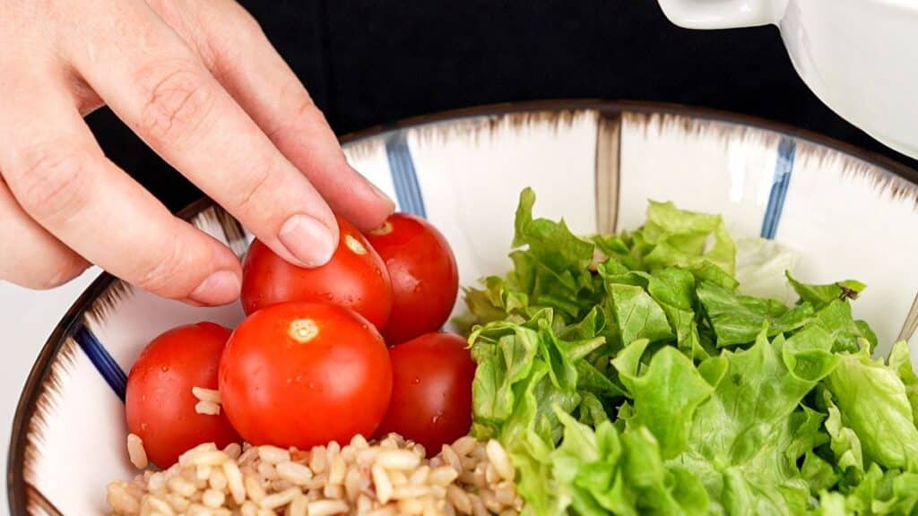 tomatoes being placed on top of rice and lettuce in large bowl