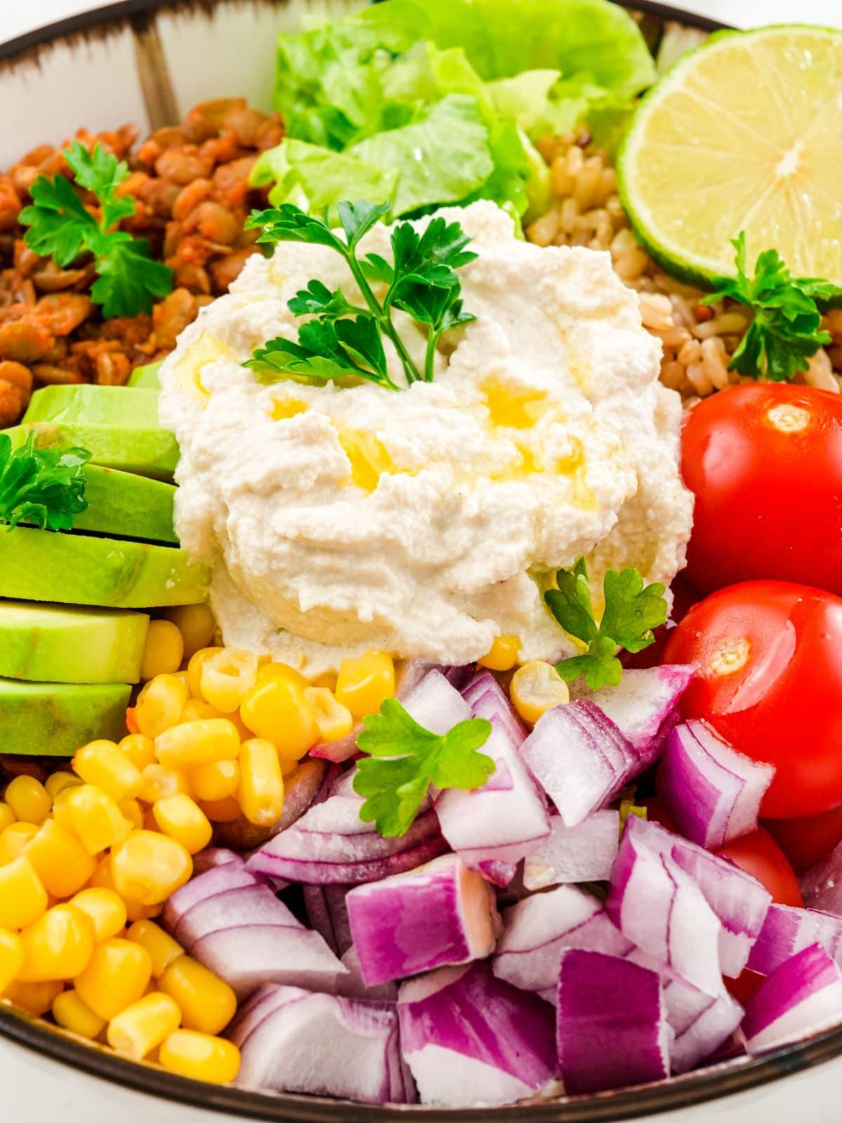 white bowl with brown rim holding vegetables topped by cream cheese