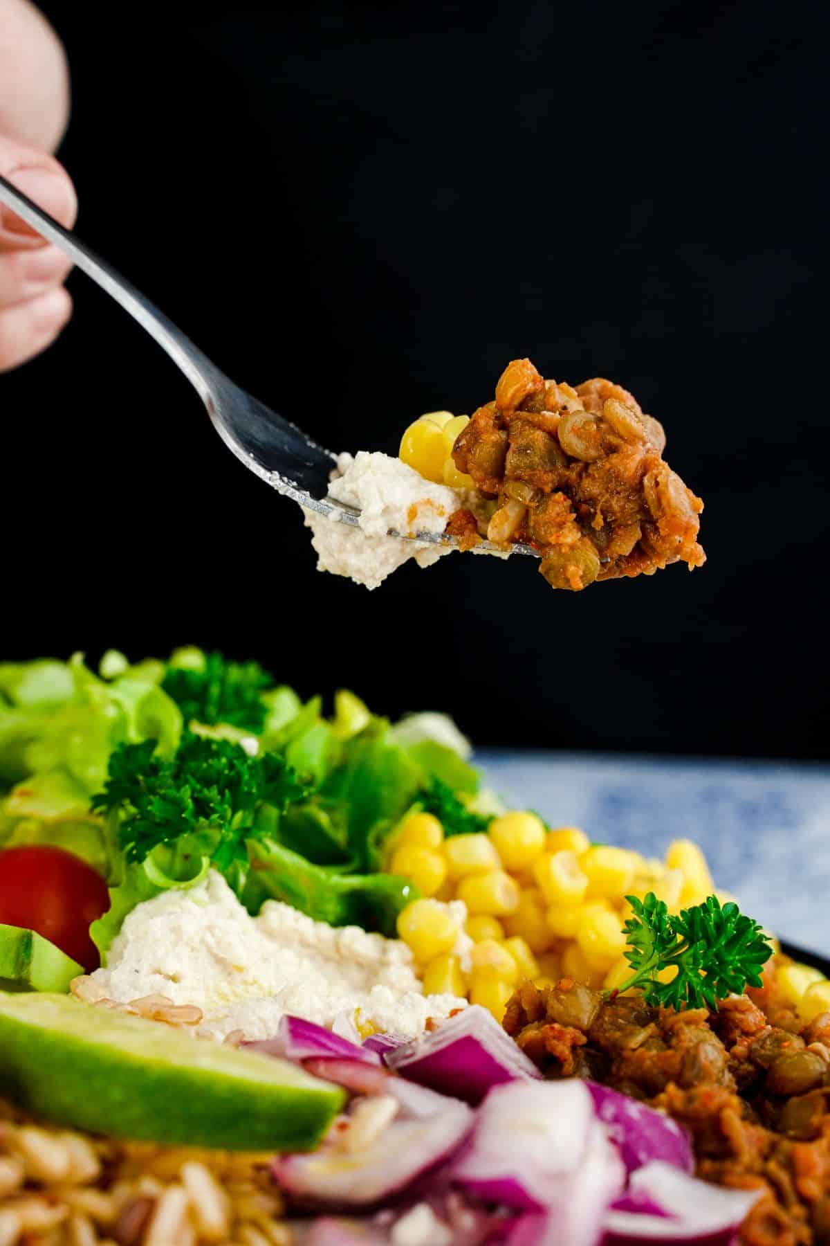 fork holding lentils from taco salad above bowl of vegetables