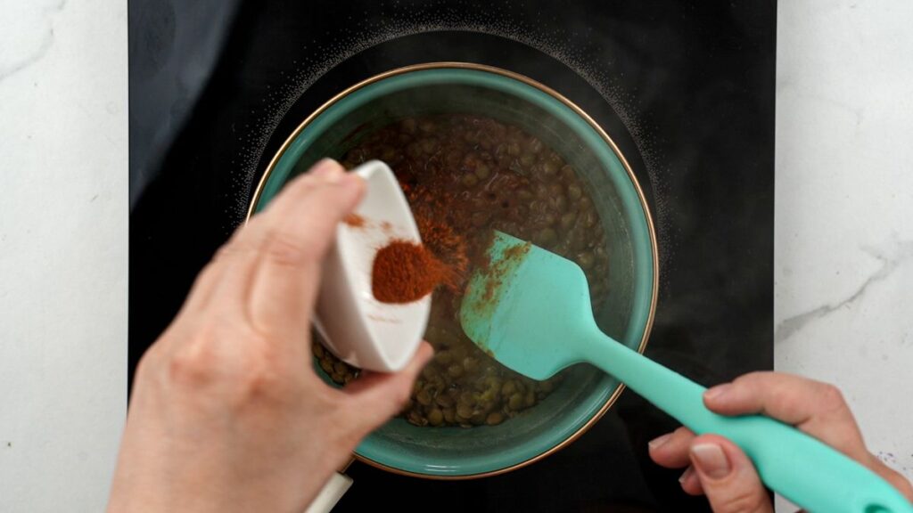seasonings being stirred into saucepan of lentils