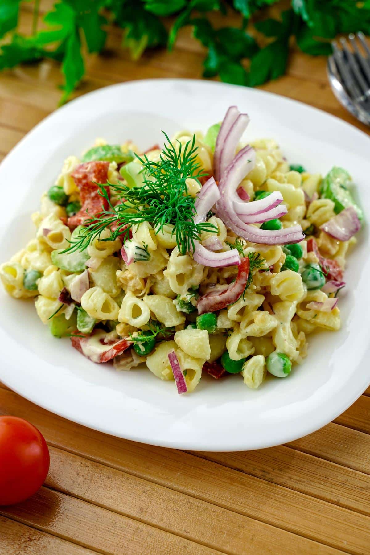 square white plate of vegan tuna pasta salad on wood table by fresh herbs