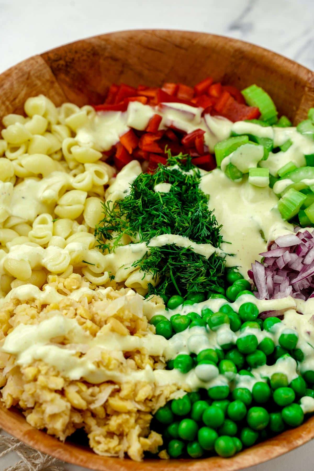 wood bowl of pasta with veggies and dressing on top