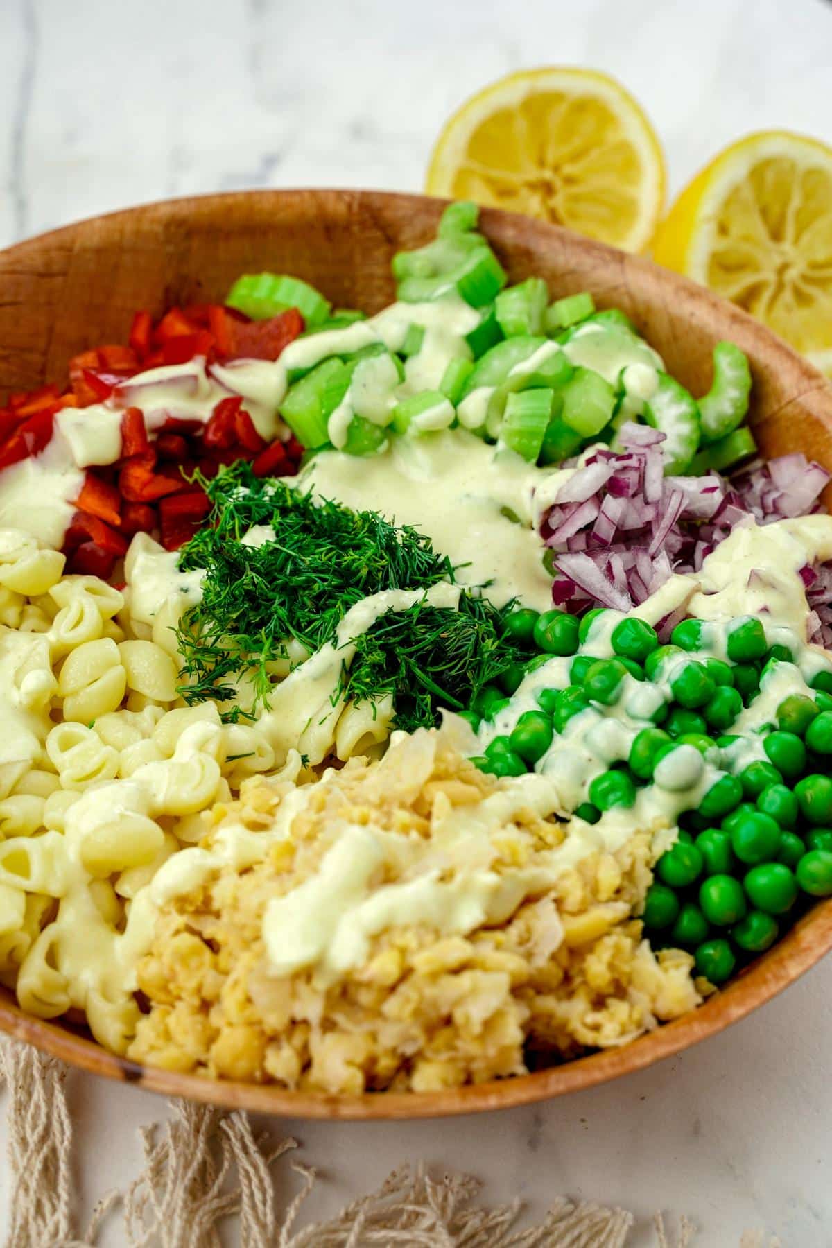 wood bowl of pasta with vegetables and dressing drizzled over the top