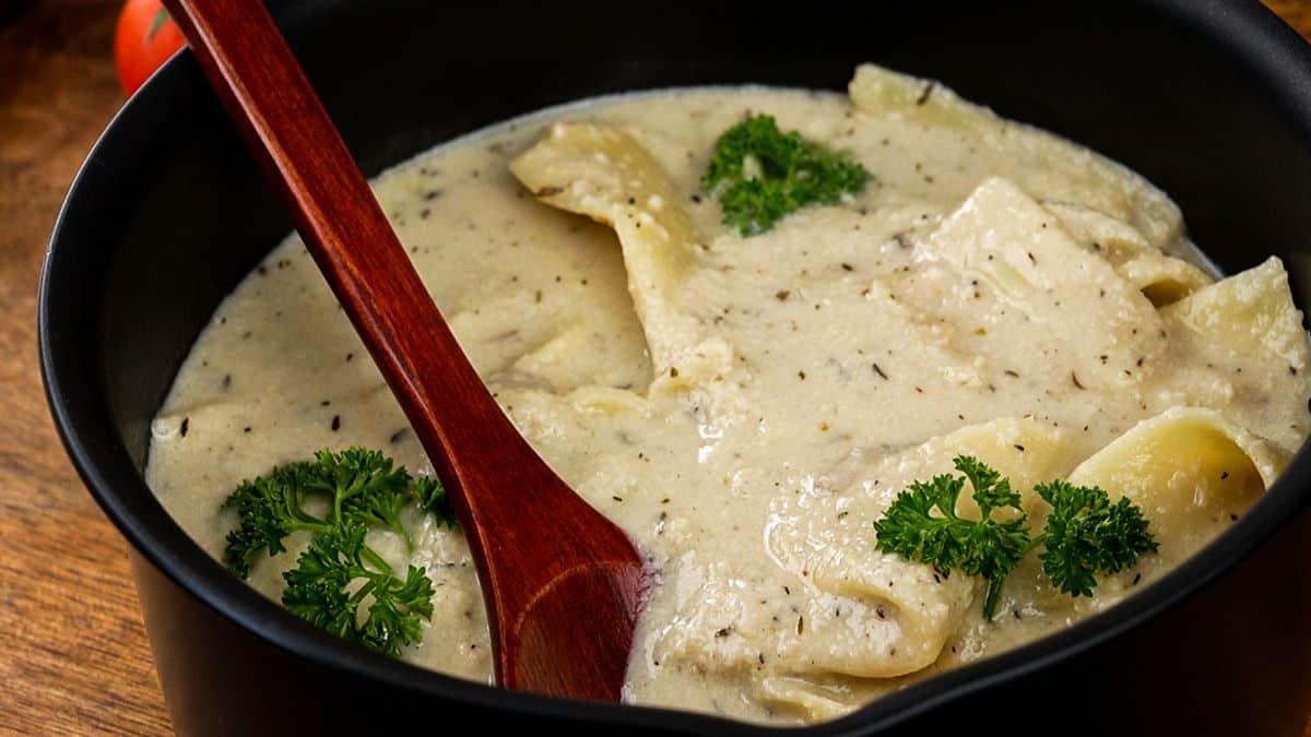 black saucepan of vegan white lasagna soup with wooden spoon in the side