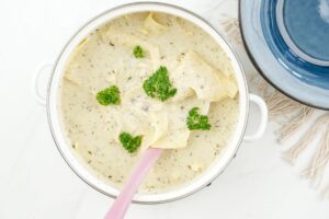 white saucepan of vegan white lasagna soup on table by blue bowl