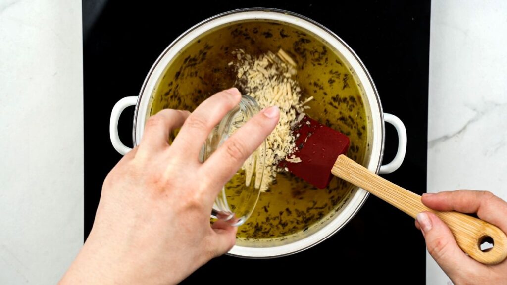 nutritional yeast being added to white lasagna soup in stockpot