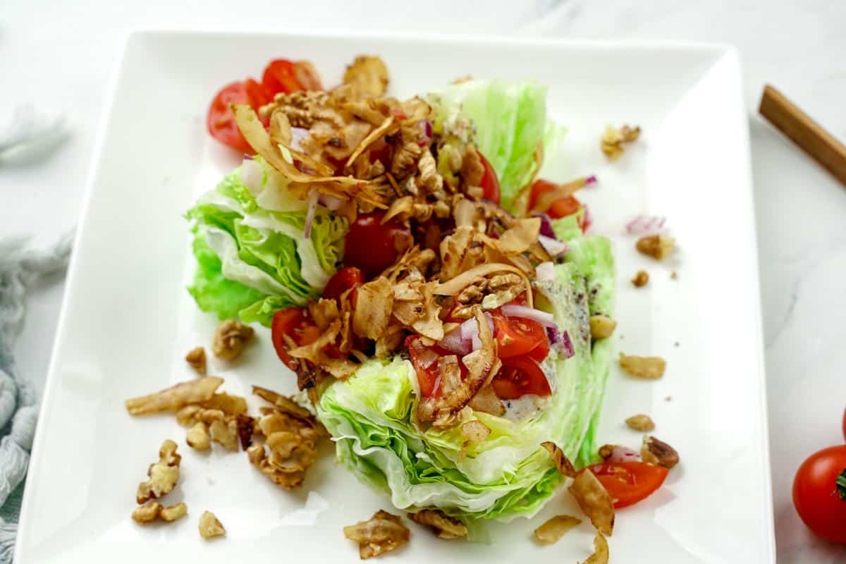 square white plate on table holding wedge salad with tomato pieces, coconut bacon, and salad dressing