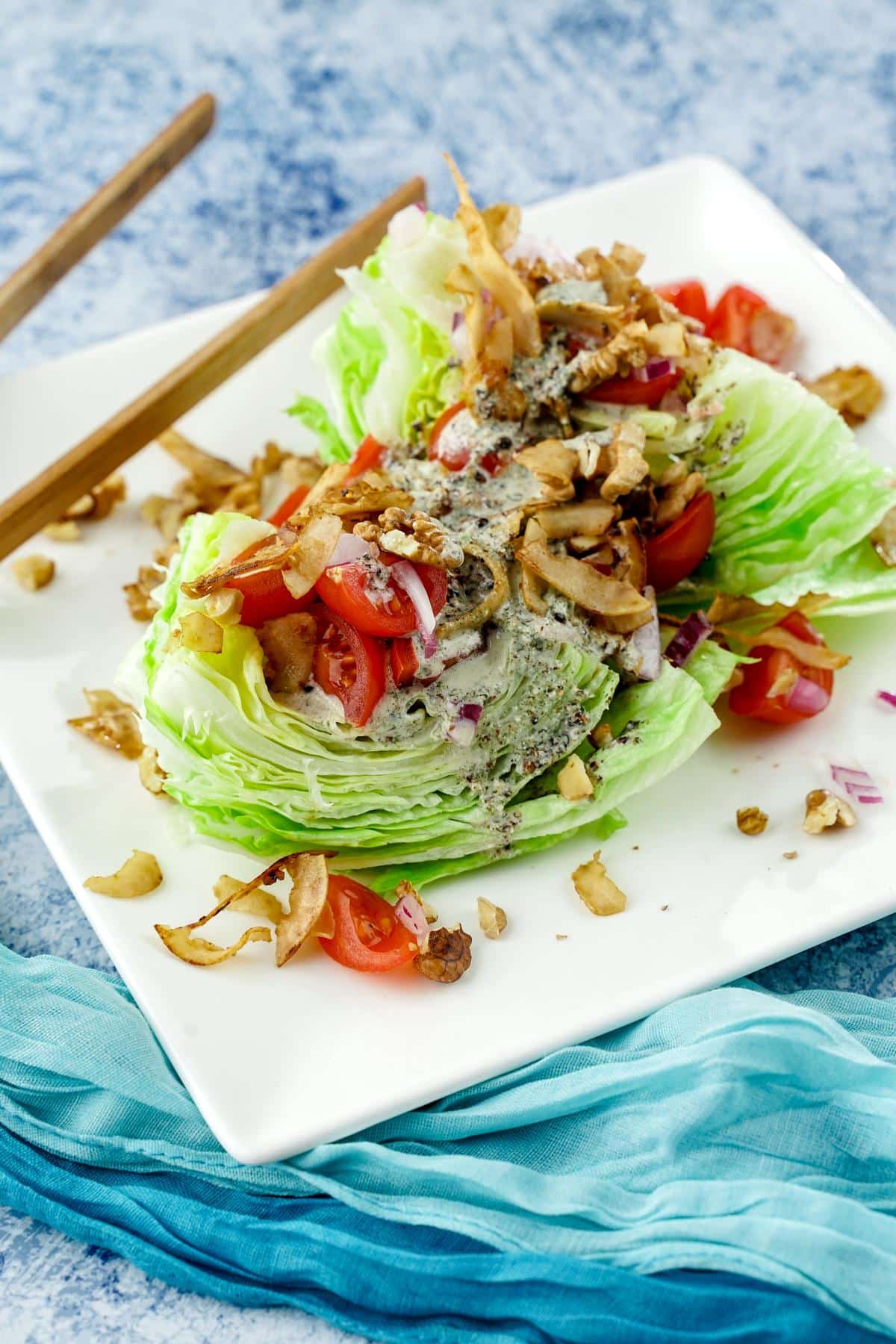 white plate holding wedge salad with tomato and coconut bacon on top sitting on teal napkin