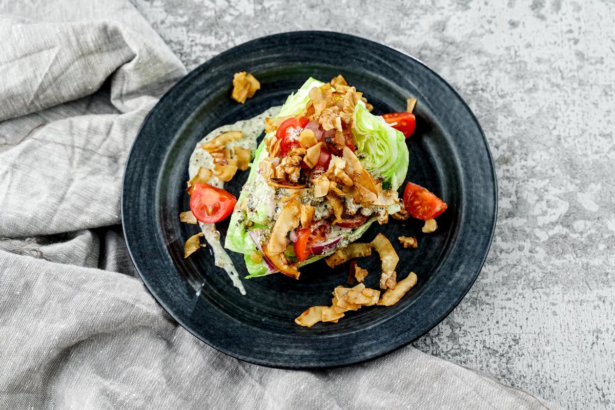 black plate holding wedge of lettuce with dressing on top of gray napkin