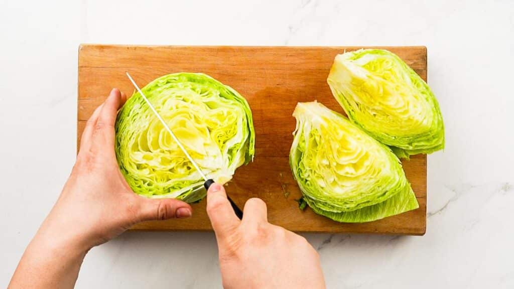 head of lettuce being cut into quarters on top of wood cutting board