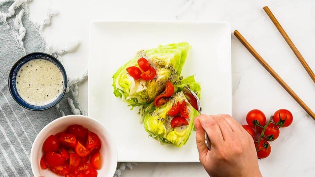 wedge of lettuce on white plate with tomatoes on top