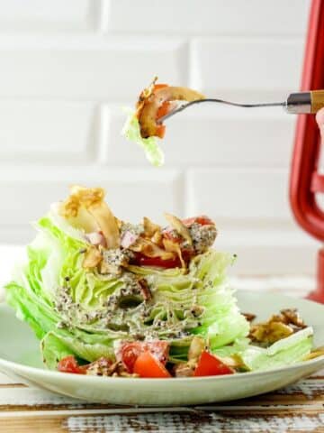 fork of coconut bacon above wedge salad on plate in front of white tile wall