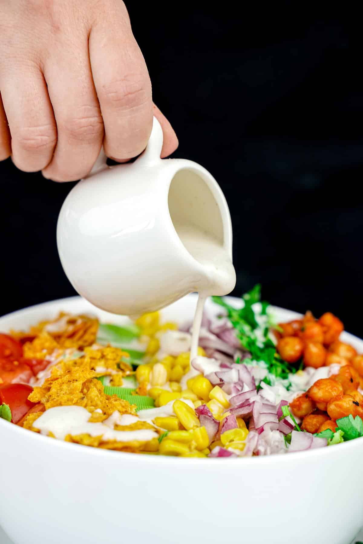 dressing in white mug being poured over bbq chickpea chopped salad in large white bowl with black background