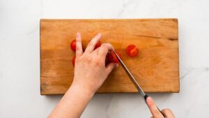 tomatoes being sliced on wood cutting board