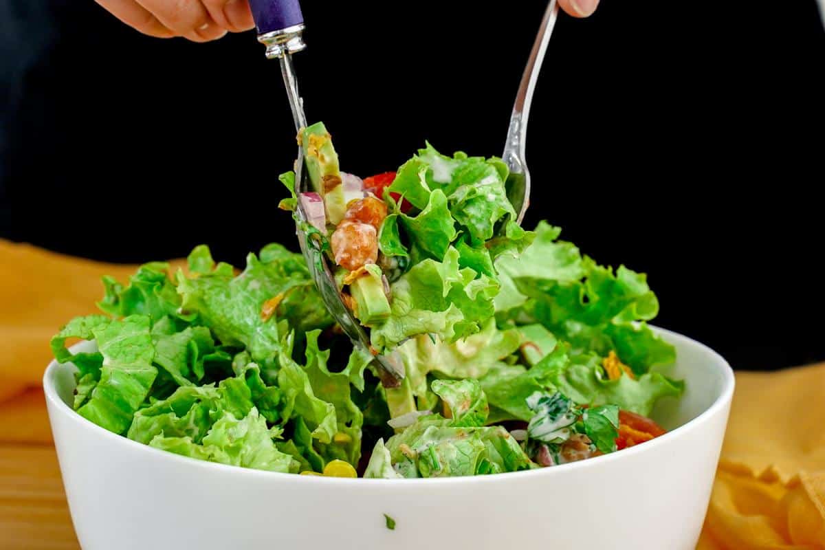 salad being tossed with forks in white bowl