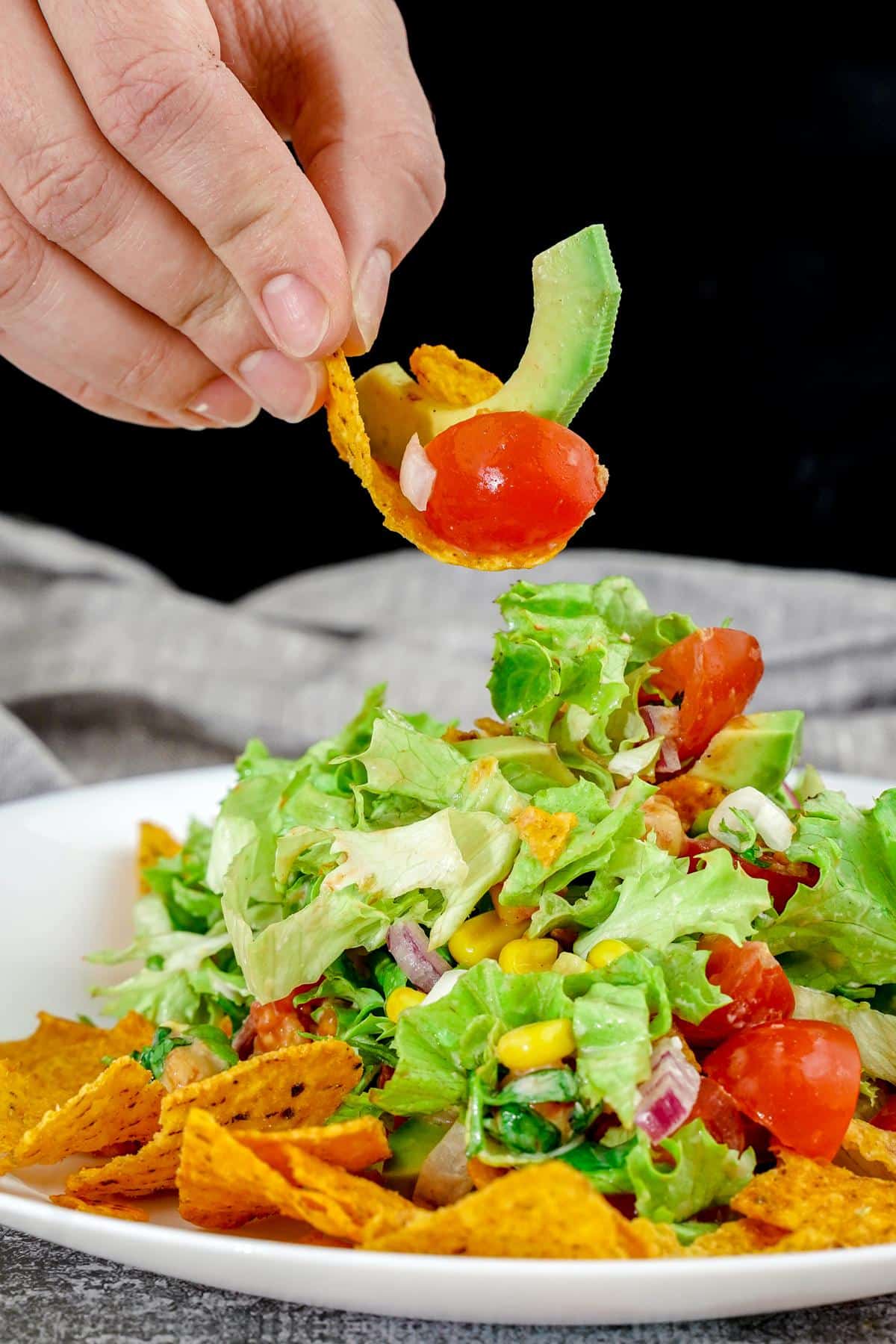 hand holding chip above bbq chickpea chopped salad in white bowl