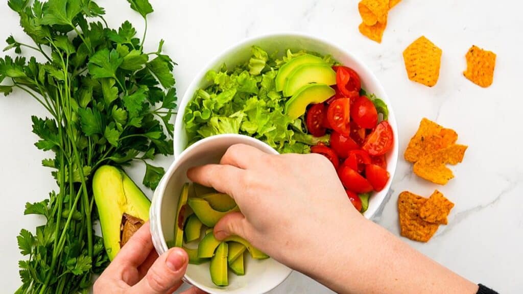 hand putting avocado slices on top of salad