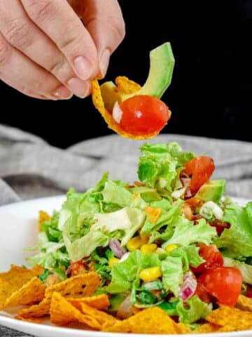 hand holding chip above bbq chickpea chopped salad in white bowl