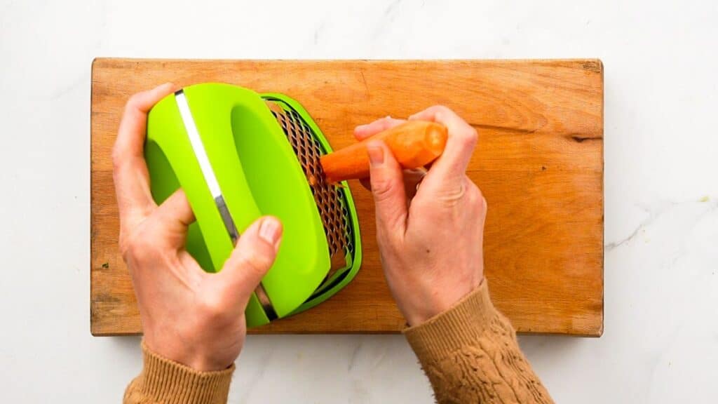 hand grating carrots over wooden cutting board