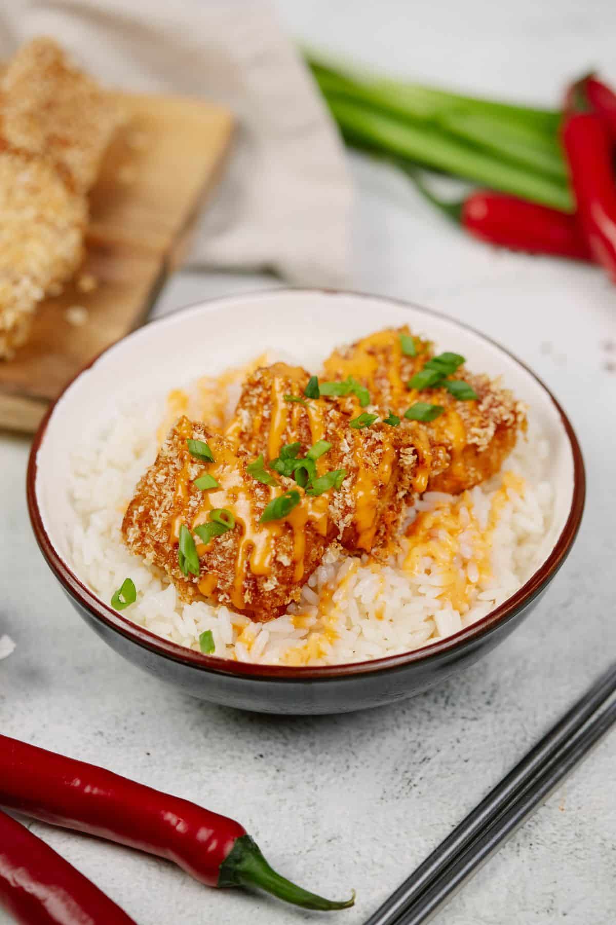 panko breaded tofu on top of bed of rice in black and white bowl