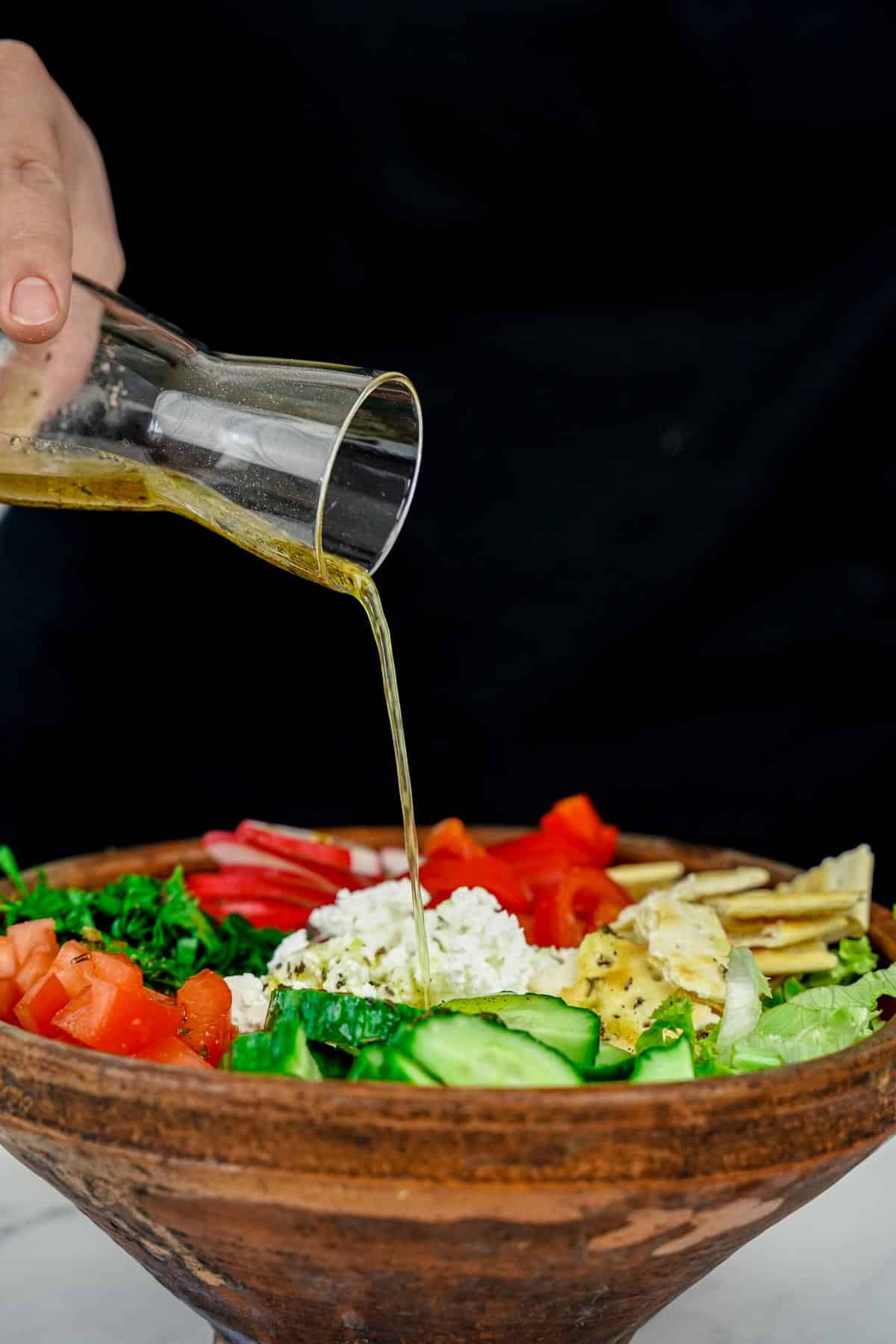dressing being poured over salad in wooden bowl
