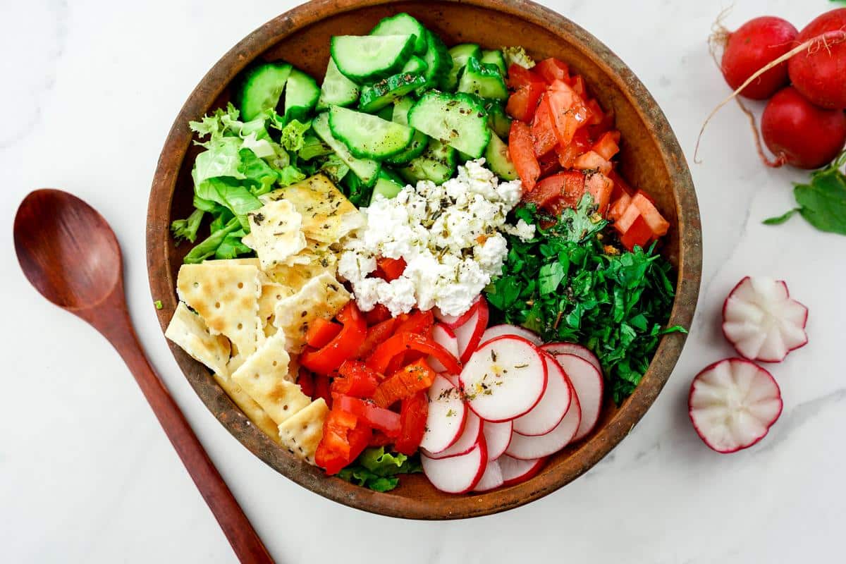 wood bowl of fattoush salad on white marble table by wooden spoon