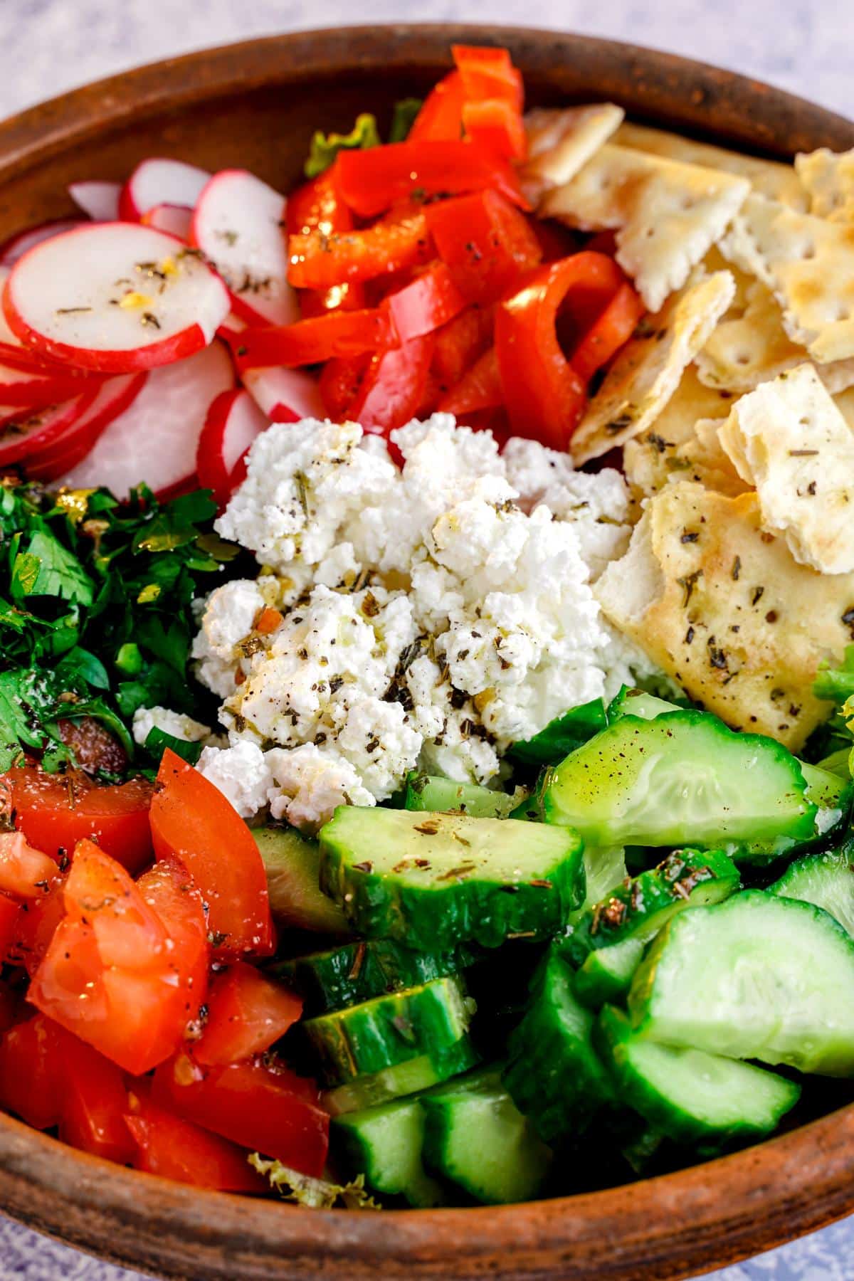 vegetables layered in wooden bowl and topped by vegan feta