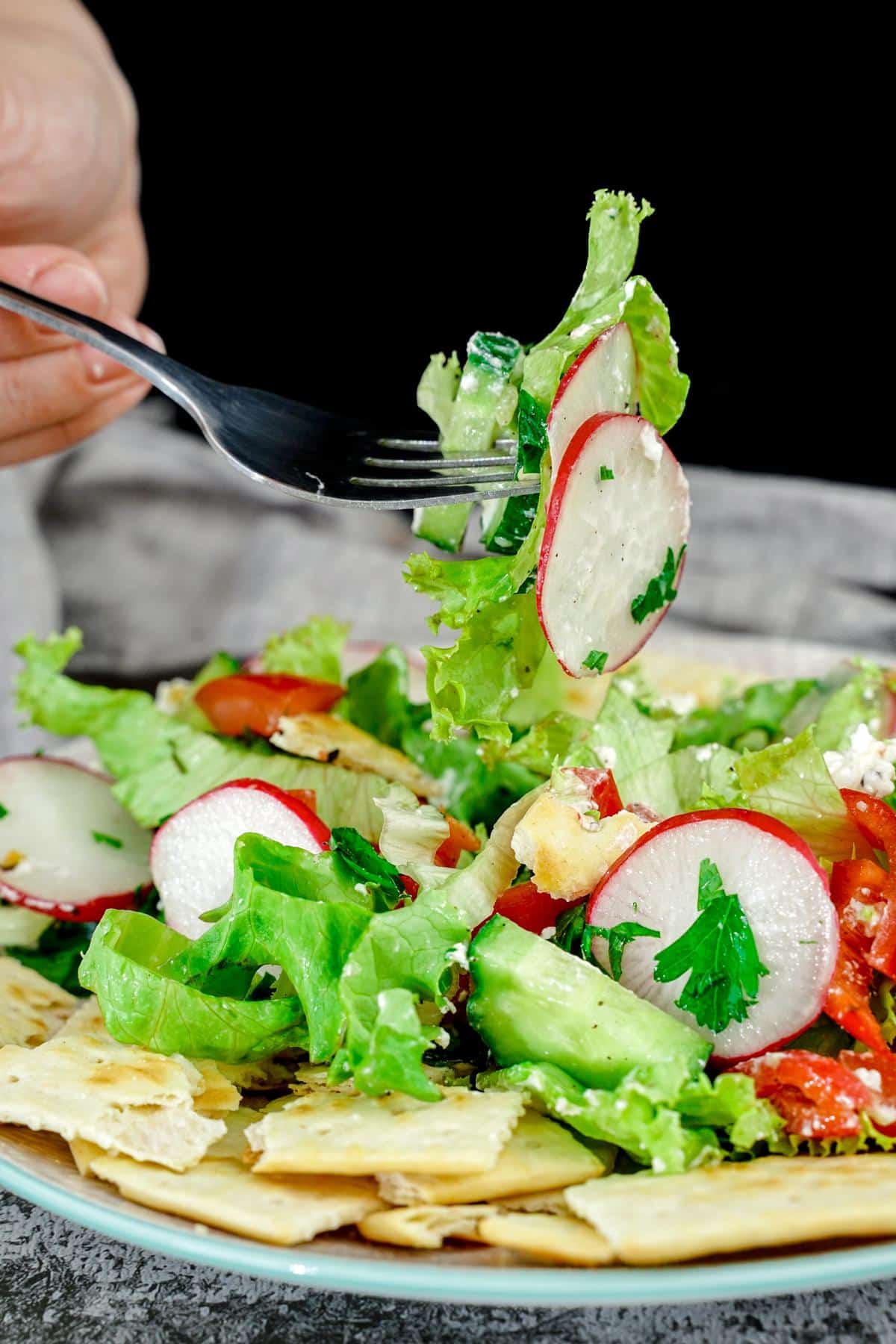 fork of fattoush salad held above blue plate on table