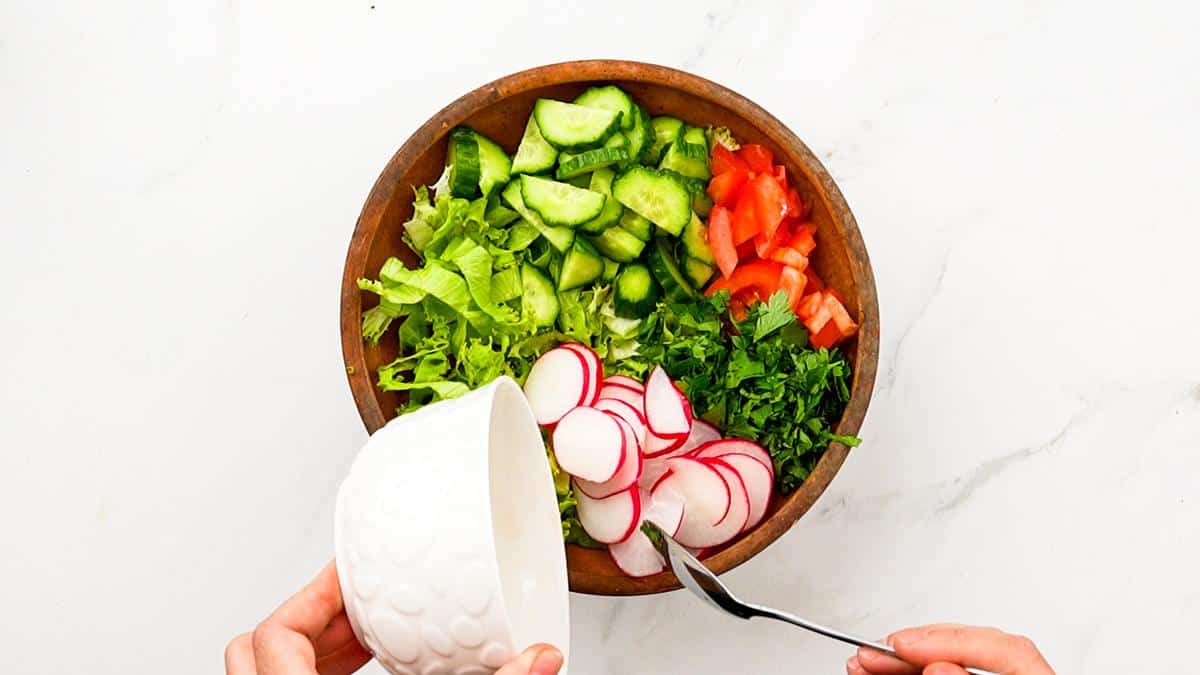 sliced radishes being poured into wooden bowl of vegetables