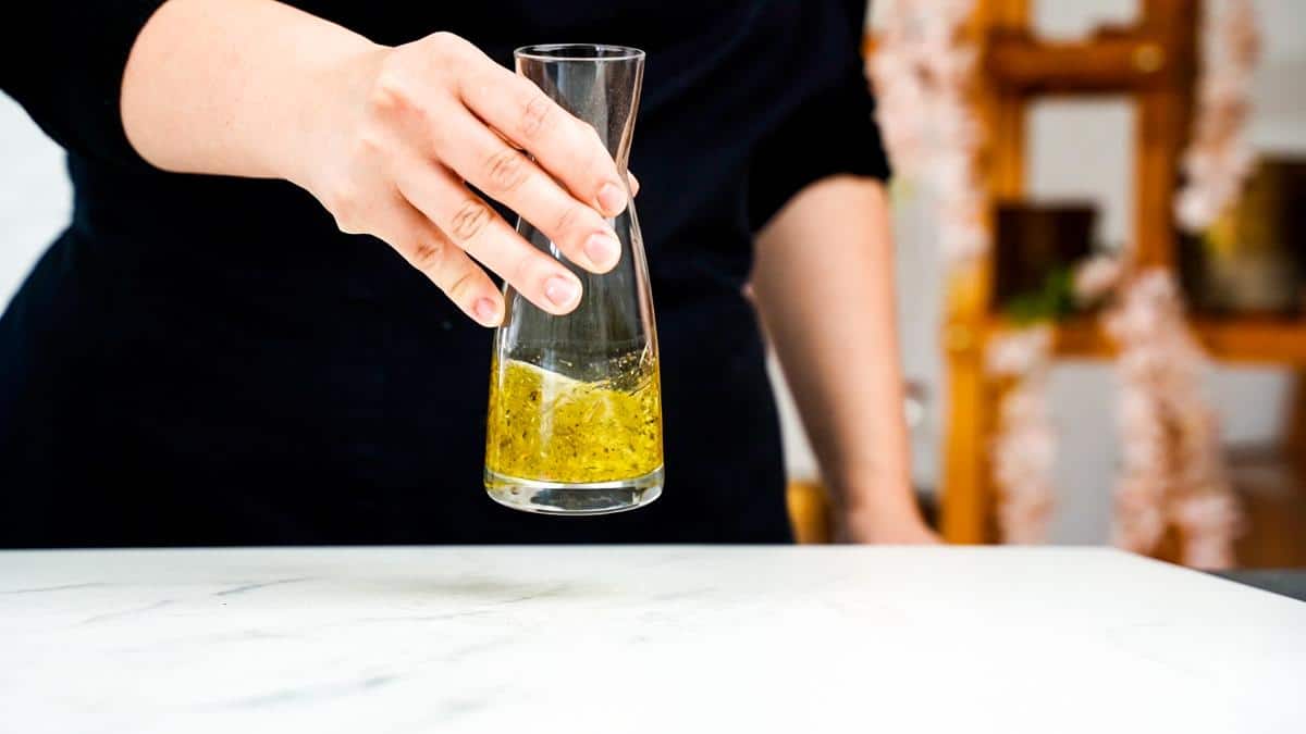 salad dressing in a glass bottle held above white table