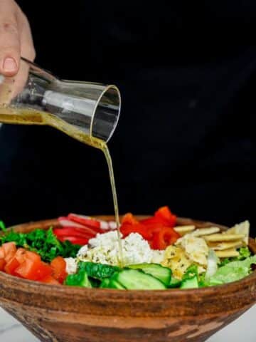 dressing being poured over salad in wooden bowl