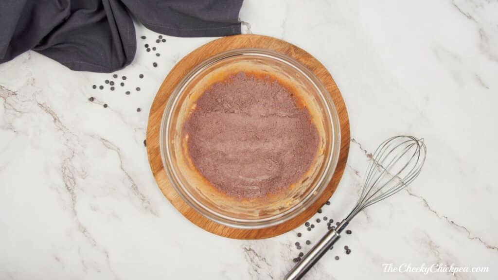 dry ingredients on top of wet ingredients in glass bowl on wood slab