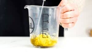 glass measuring cup of oil being whisked