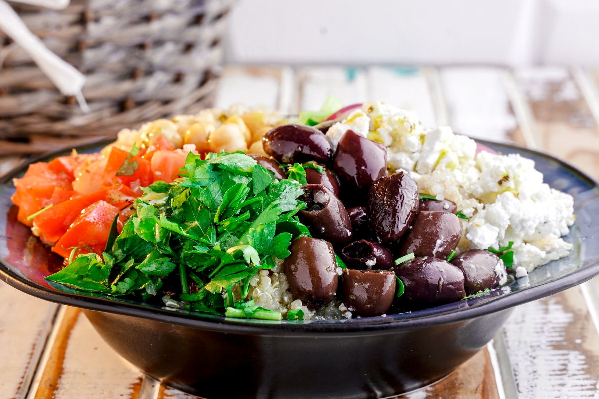 black bowl packed with ingredients for Greek quinoa salad