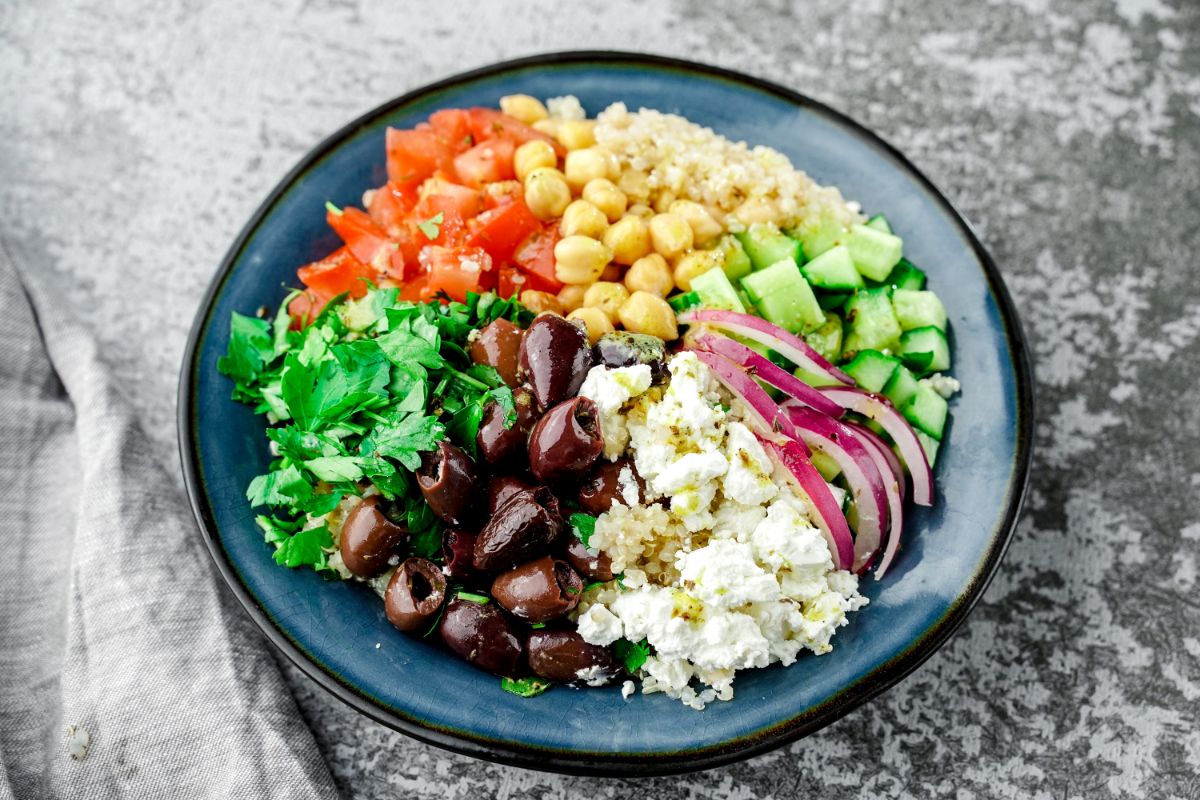 blue plate of quinoa salad ingredients on grey tablecloth