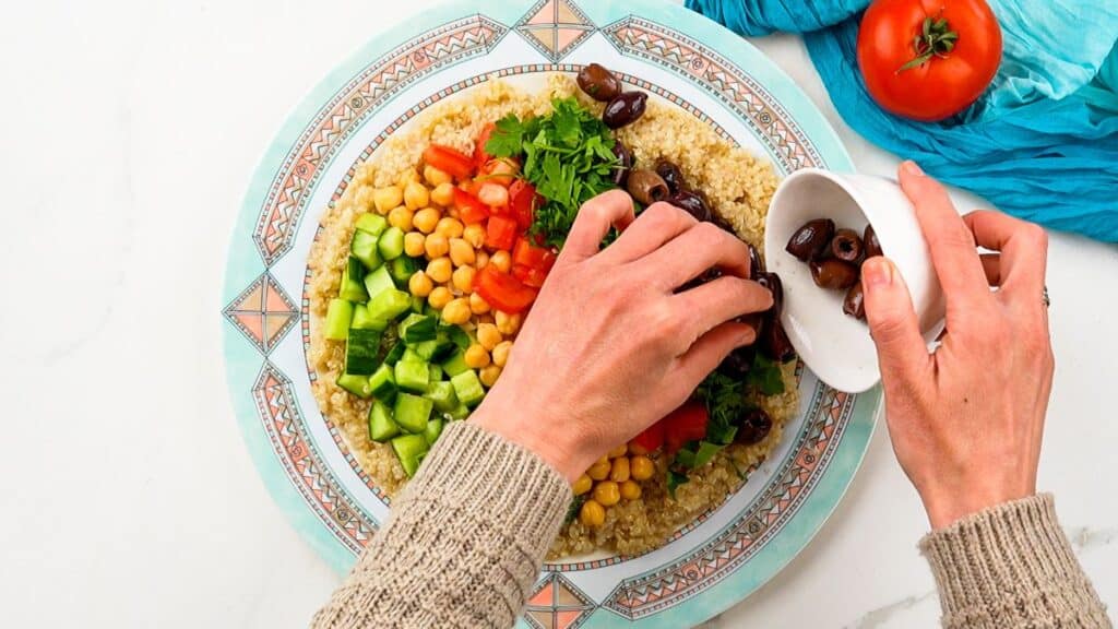 hand putting olives on plate of couscous and vegetables