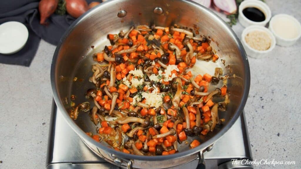 minced garlic on top of cooked carrots and mushrooms in skillet