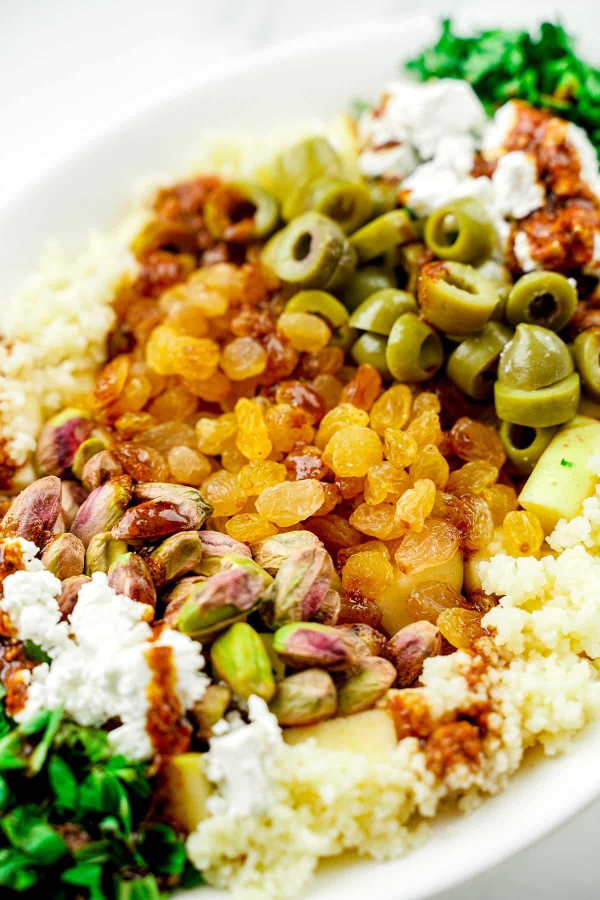 golden raisins and green olive slices on top of a bed of couscous in white bowl