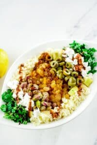 white bowl of moroccan couscous salad with green olives and fresh herbs on top