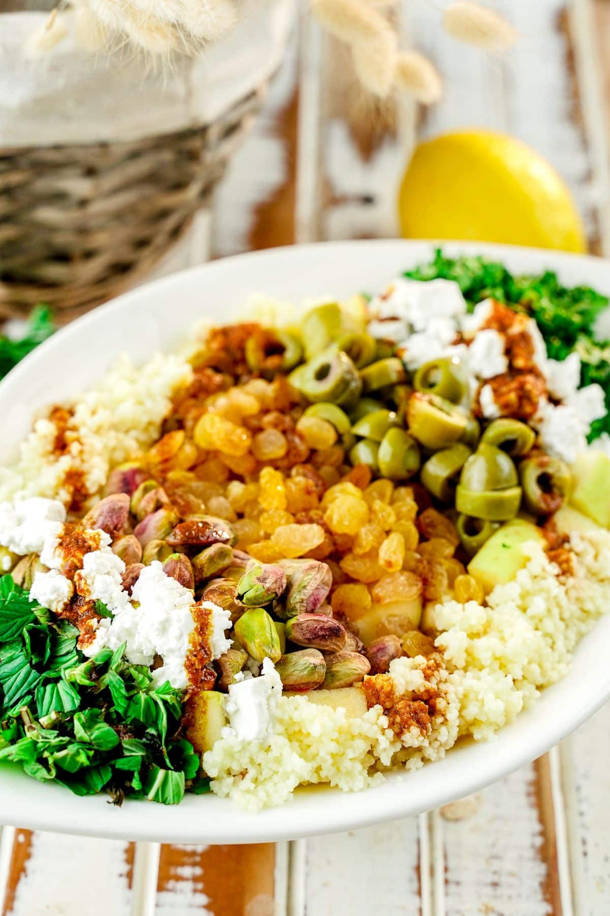 couscous salad with olives and nuts in white platter topped with fresh herbs and vegan feta