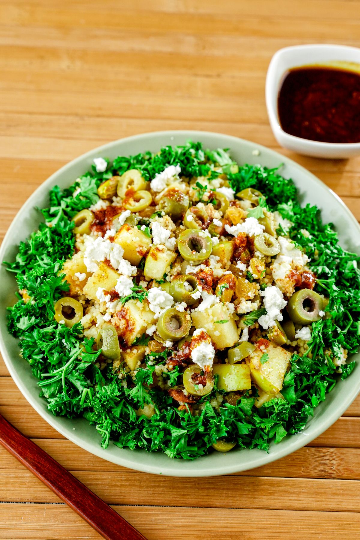 large white bowl of Moroccan couscous salad with fresh herbs on wood slat table with wooden spoon