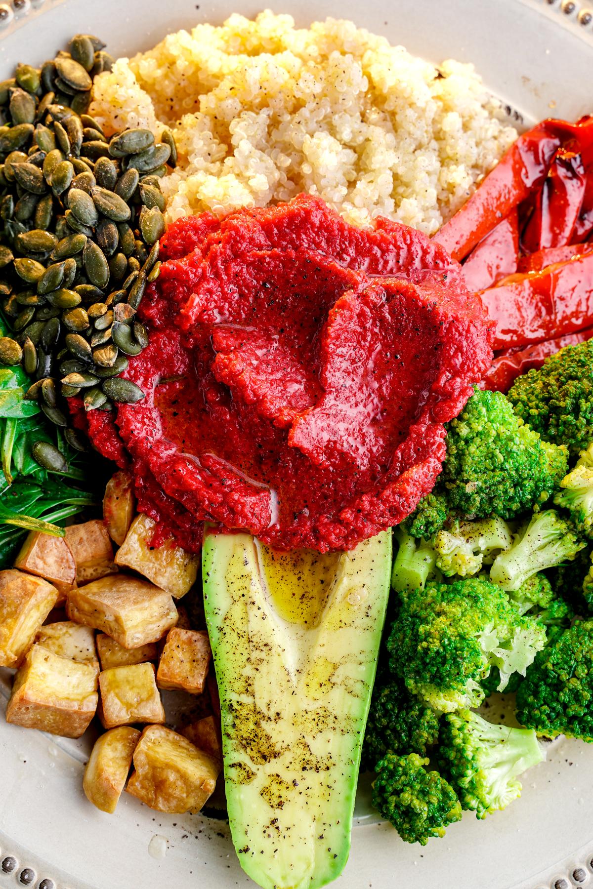 beet hummus on top of tofu, broccoli, and quinoa in bowl