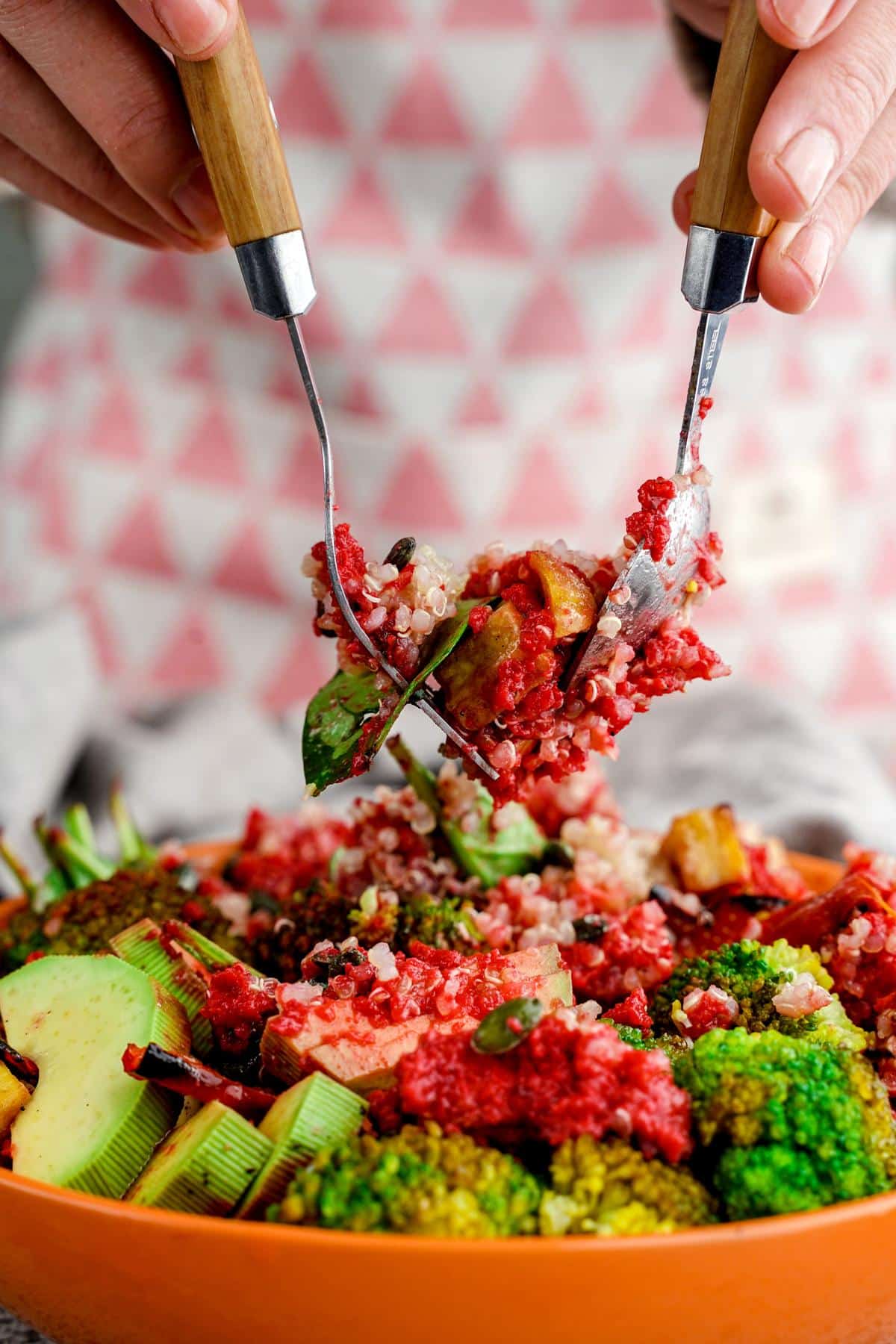 salad being tossed in orange bowl with forks