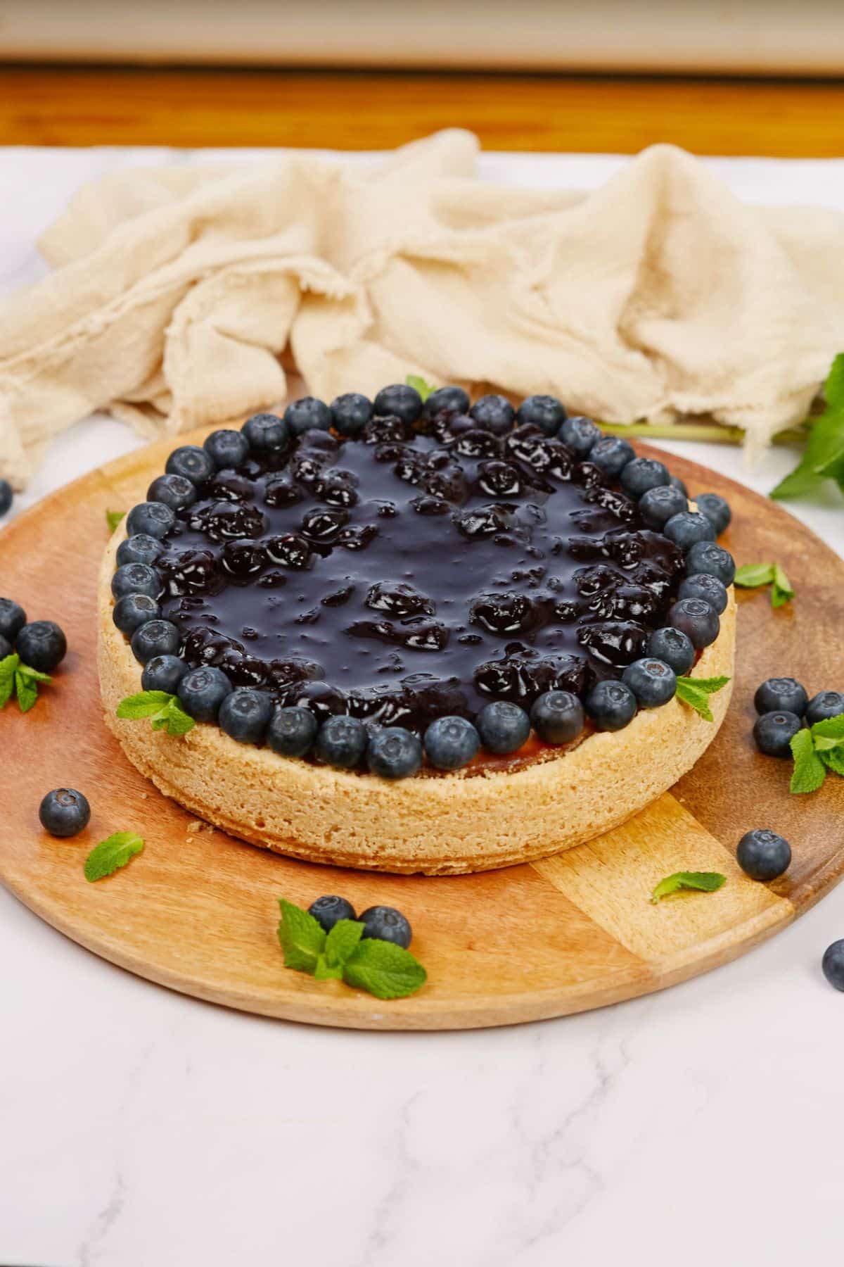 round wood board on table holding vegan cashew cheesecake that has been topped by blueberries