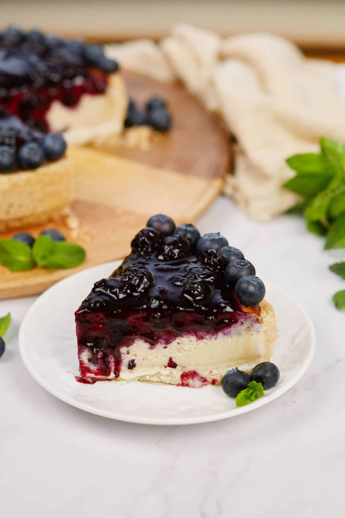 slice of vegan cashew cheesecake on white plate topped by blueberries